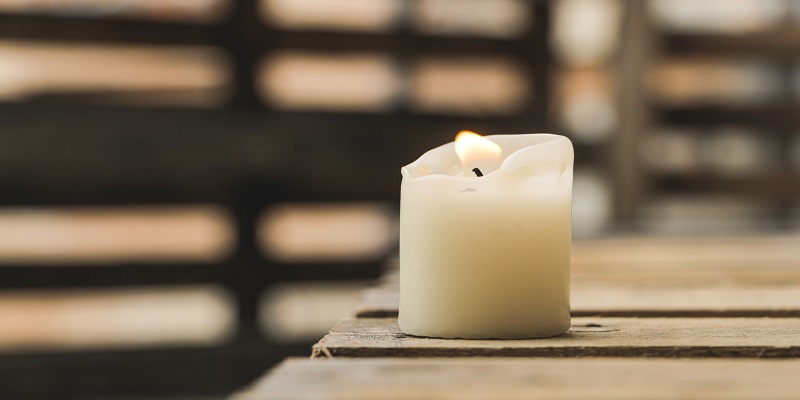 White memorial candle on rustic wood table symbolizing cremation services and quiet remembrance